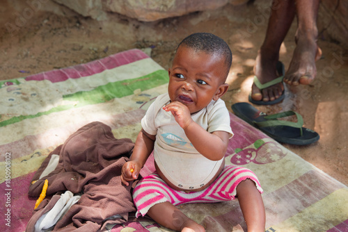 Foto village single african child crying sitting on the ground on a blanket, eating food in the dirt