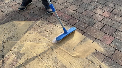 Woman brushes sand between paving blocks to maintain a pathway, England