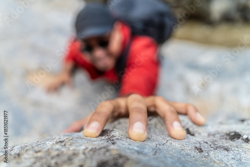 Handsome asian hiker climber carefully grips a rock while scaling a steep cliff during a hike in a national park.