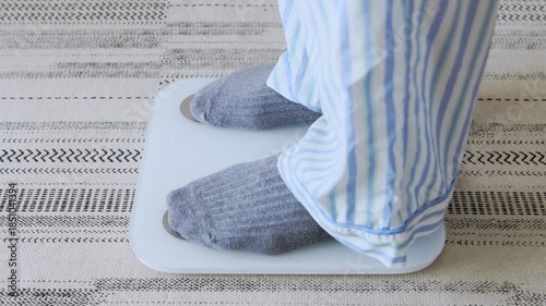 Person in pajamas steps off a weight scale with a measuring tape, achieving a weight loss goal