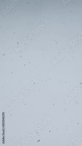 Falling snow from above. Snowfall. Snow falls in flakes vertically from above against sky.