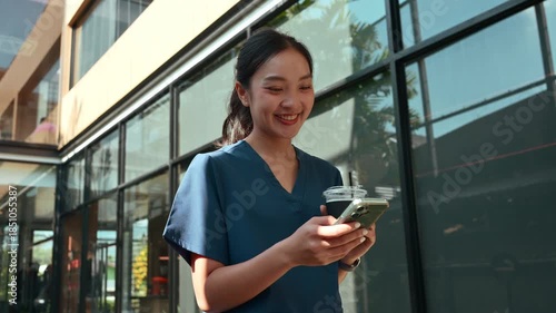 Young female doctor in scrubs using her smartphone during a coffee break. Cheerful medical professional scrolling on her phone