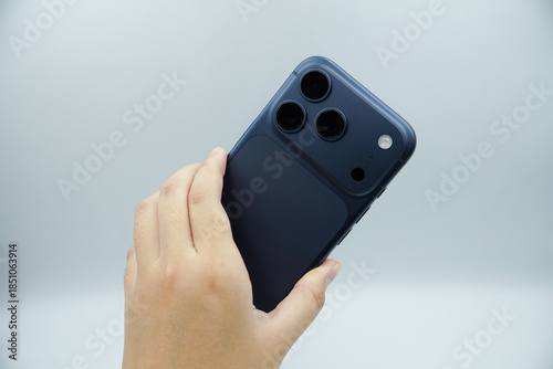 Hands holding an expensive smartphone in the deep blue variant and showing the back of the smartphone with a white background