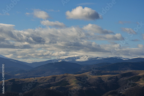 mountain landscape view from hill in winter season with small wood cabins and low clouds on blue sky