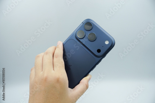 Hands holding an expensive smartphone in the deep blue variant and showing the back of the smartphone with a white background