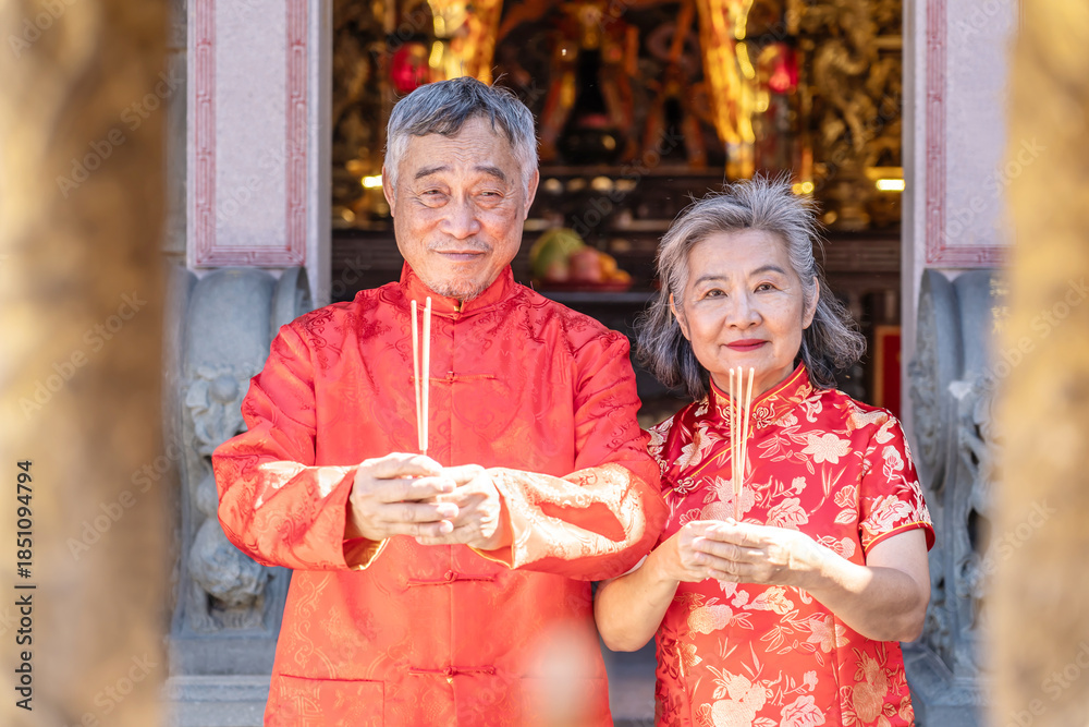 Obraz premium Celebrating Lunar New Year 2026 with cultural pride and warm greetings at a temple by a asian senior couple dressed in bright red traditional outfits expresses heartfelt wishes