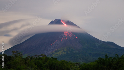 Photos Red glowing lava flowing down the slopes of Mount Merapi while thick clouds swirl and cover the upper volcano