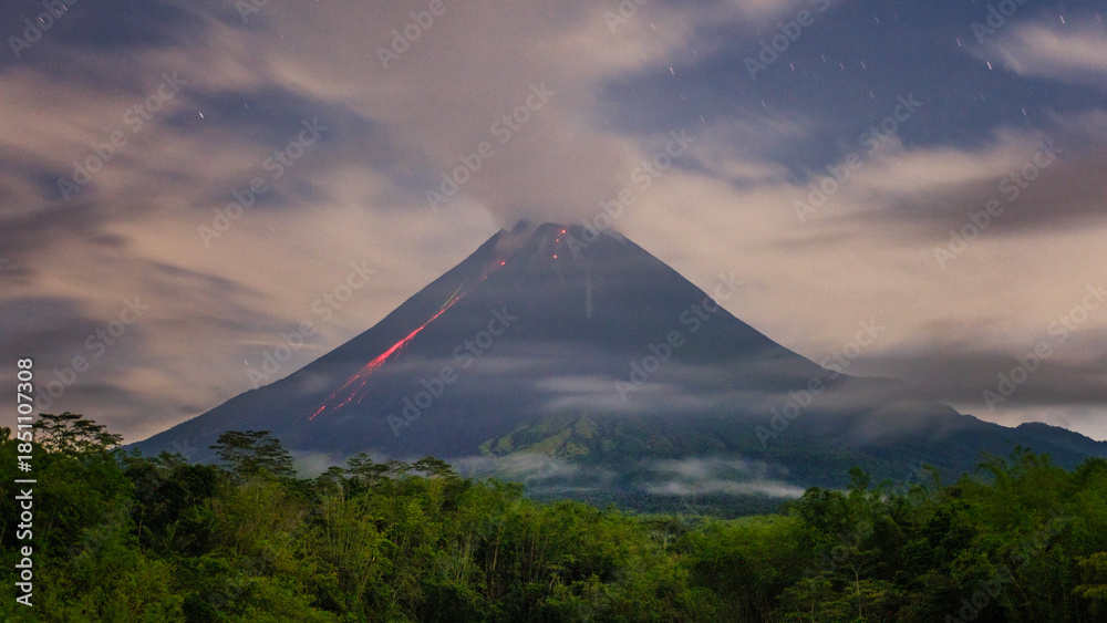 Fototapeta premium Active Volcano at Night With Glowing Lava Flow and Low Clouds