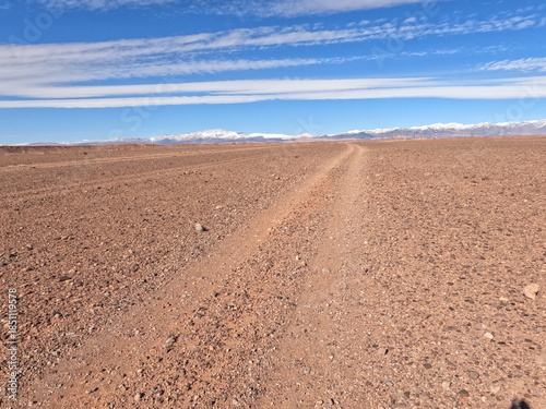 Dirt road in the desert under a blue sky with layered clouds