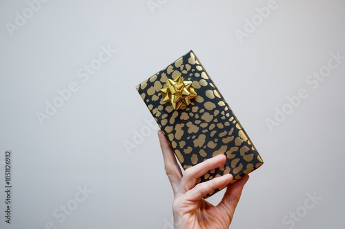 Hand holding a gift. Black and gold paper gift with a shiny gold bow present hold in hand.