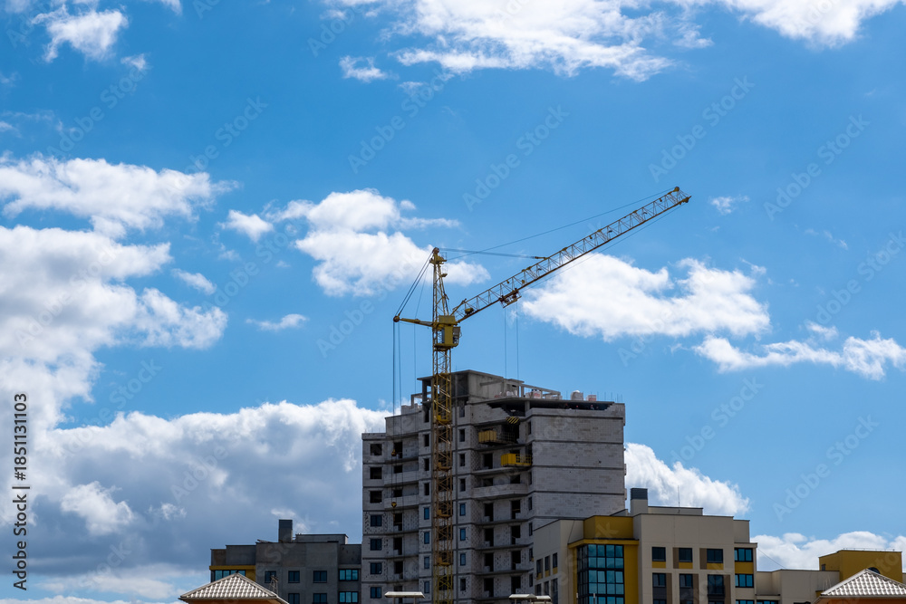 Fototapeta premium Tower Crane and Apartment Building Under Construction Against Cloudy Sky