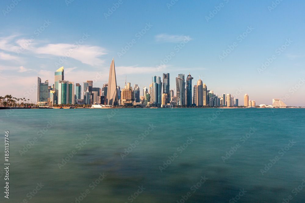 Fototapeta premium Panoramic view of West Bay in Doha Skyline Over Calm Sea: Modern Cityscape With Tall Buildings And Blue Sky