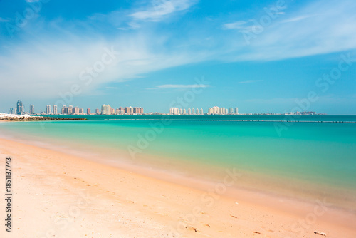 Panoramic view of The Pearl Island in Doha bright sunny beach with turquoise sea and distant city skyline under clear blue sky