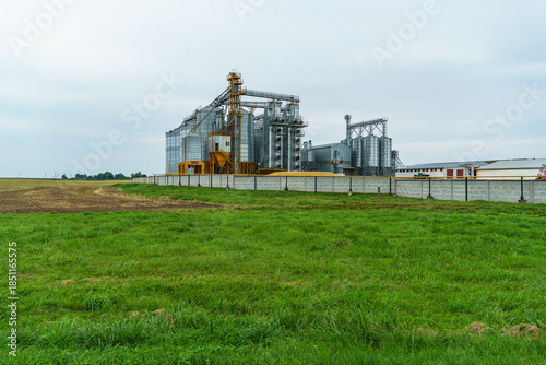 A large modern plant located near a wheat field for the storage and processing of grain crops. view of the granary illuminated by the light of the setting sun against the blue sky. harvest season.