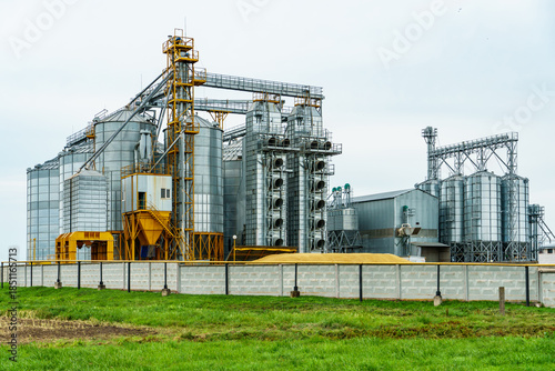 A large modern plant located near a wheat field for the storage and processing of grain crops. view of the granary illuminated by the light of the setting sun against the blue sky. harvest season.