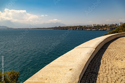 Curved stone parapet overlooks the sea at Karaalioglu Park, offering a view of the blue Mediterranean and Antalya's distant rocky coast under a sunny sky. Antalya, Mediterranean, Turkey.

