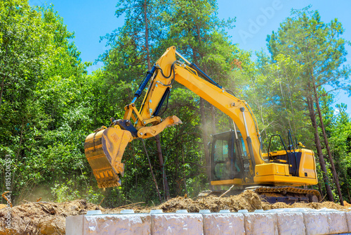 Large excavator is working to dig soil in forested area under construction site