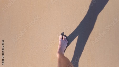 Men's legs walking on a sandy beach towards the sea