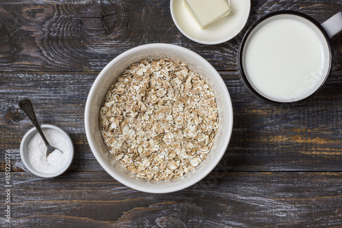 Raw four grain flakes in a ceramic bowl with milk, butter and salt arranged on a rustic wooden table, showing natural ingredients for healthy porridge