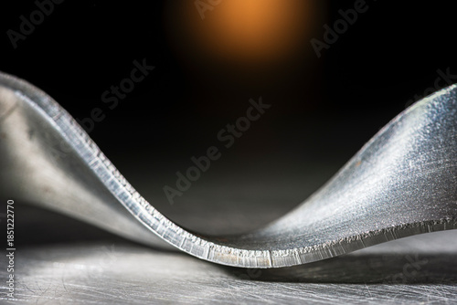 Bent steel flat bar like a ribbon, close-up of metal texture, cold, dark industrial atmosphere