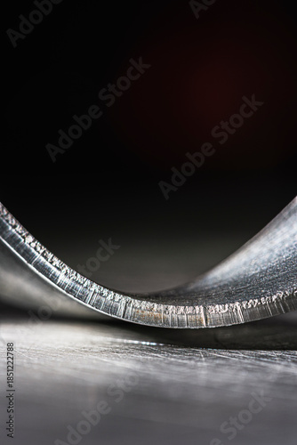 Bent steel flat bar like a ribbon, close-up of metal texture, cold, dark industrial atmosphere