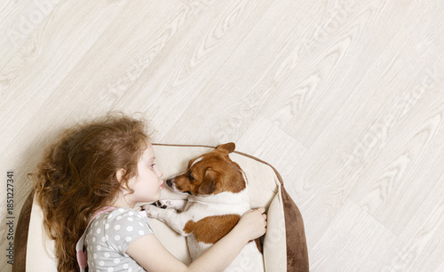 Cute girl hugging and kissing a dog, lying on wood floor.