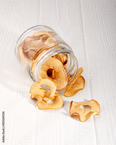 dry apples pouring out of a glass jar on a white table