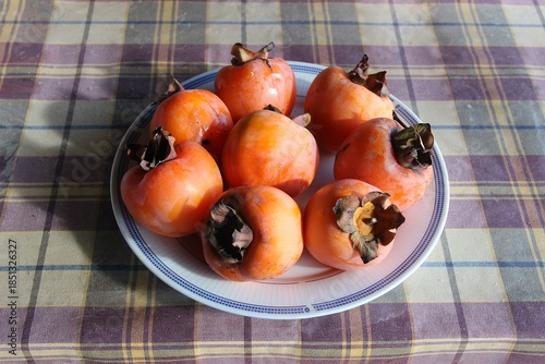 A plate of fresh ripe orange persimmon fruits on a checkered tablecloth