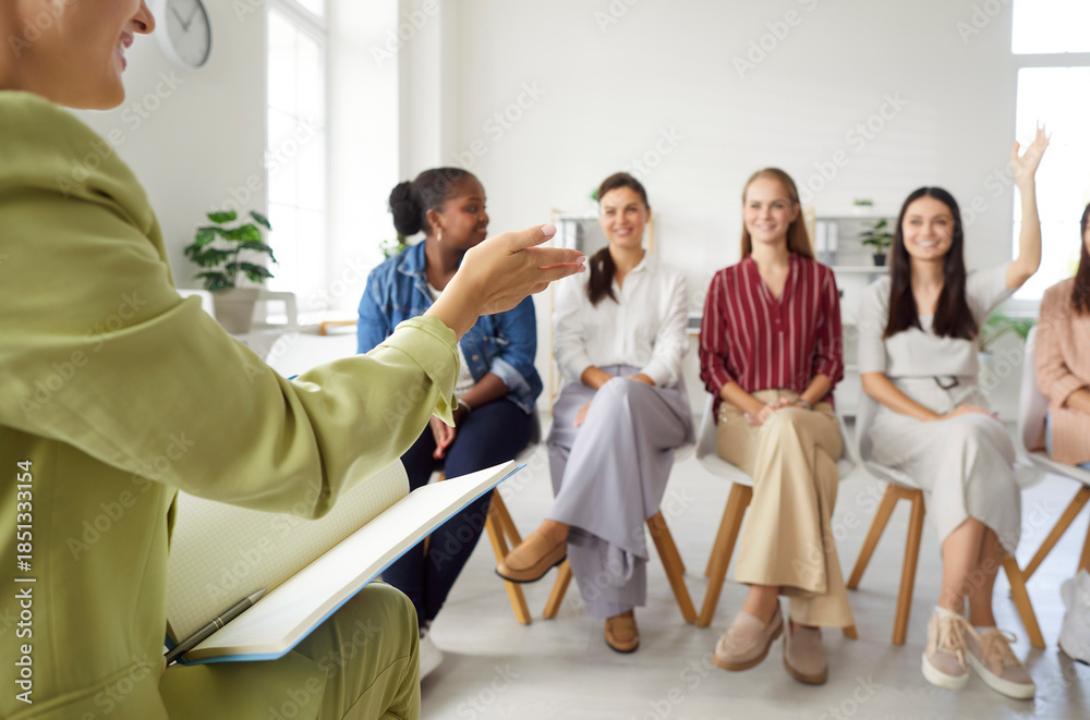 Obraz premium Group of diverse women meeting and communicating with a professional business coach. Team of happy young multiracial ladies sitting in an office, discussing ideas and asking questions