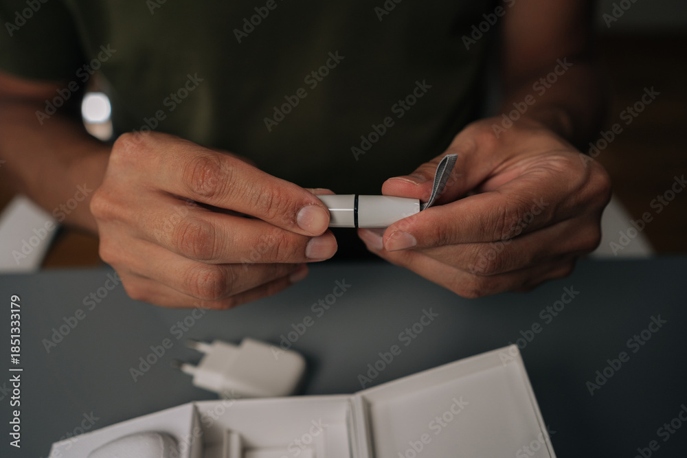 Obraz premium Close-up cropped shot of unrecognizable man sitting at table unpacking new electronic cigarette from box, holding heating element and cover. Concept of modern alternative to traditional smoking.