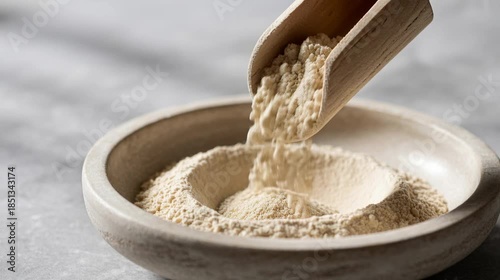 cinematic macro shot of neutral beige protein powder or organic flour pouring from wooden scoop into stone bowl on light grey background for healthy nutrition and baking concept