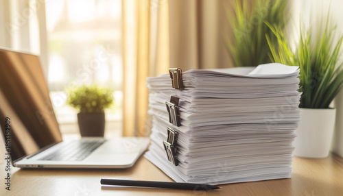 Large stack of documents with binder clips on office desk.