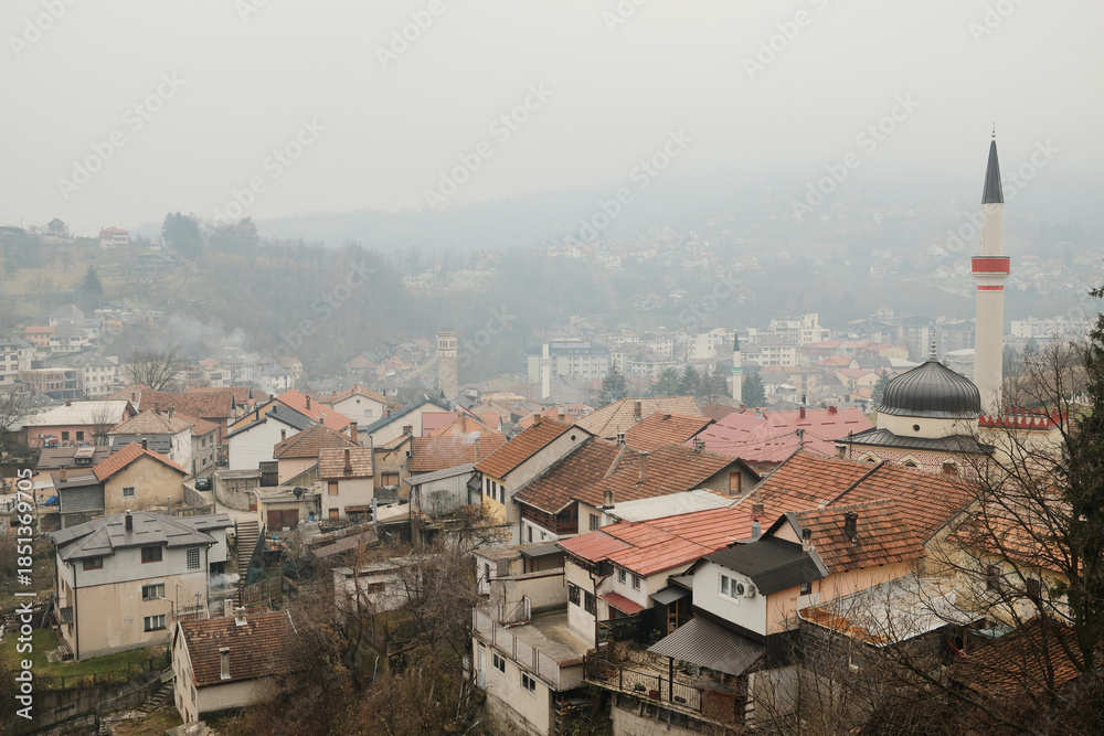 Fototapeta premium Foggy panoramic view of Travnik city in Bosnia and Herzegovina with traditional houses and mosque minaret seen from Travnik Fortress.