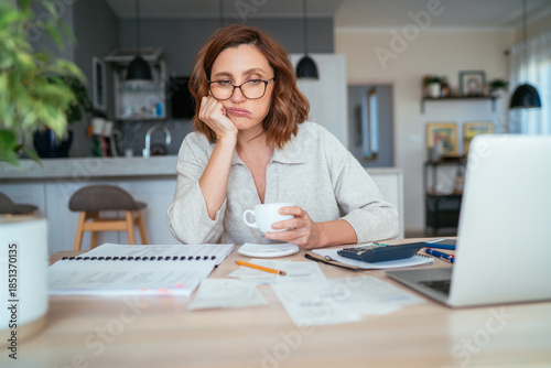 Fotografi Beautiful middle-aged woman in glasses thinking about family business budget gazing at monthly bills and documents at home living room office