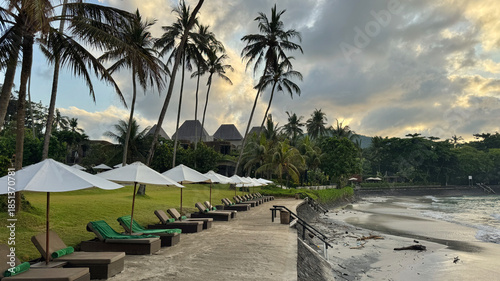 Row of white umbrellas and lounge chairs in front of the beach and the sea in Bali, Indonesia