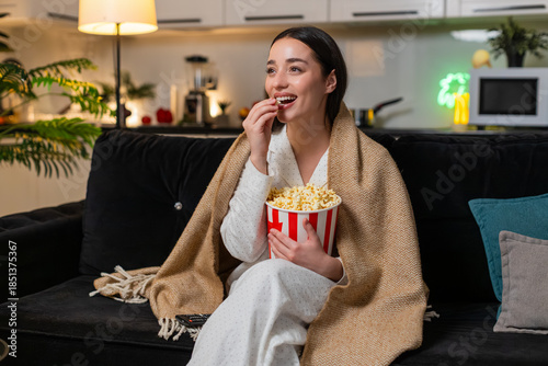 Принти на полотні Young woman at night home watches tv or online stream laughs out loud munches popcorn happy mood late