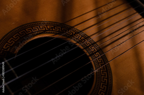 Close-up photo of an acoustic guitar with shadows. Guitar strings, neck, frets and body