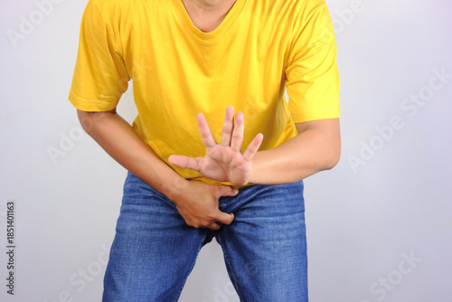 Obraz na plátně A man in a yellow shirt with one hand covering his crotch with the other in a stop or surrender gesture