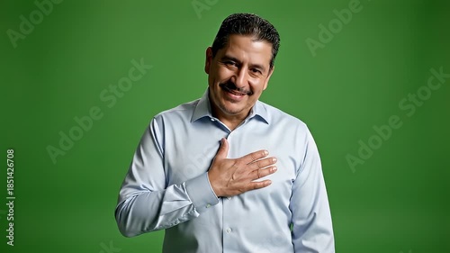 Man Showing Respect with Hand on Heart Against Green Background.