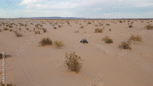 Aerial view of Polaris RZR UTV driving through desert sand dunes at sunset.