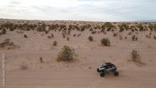 Aerial view of Polaris RZR UTV driving through desert sand dunes at sunset.