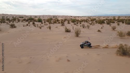 Aerial view of Polaris RZR UTV driving through desert sand dunes at sunset.