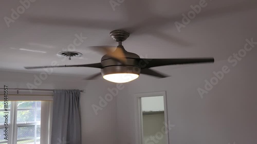 Modern silver ceiling fan with light on spinning smoothly at medium speed indoors