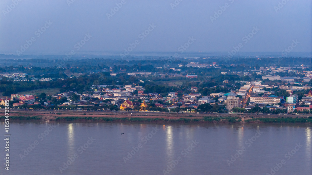 Obraz premium Aerial drone view of Savannakhet city lights turning on at twilight. The street lights illuminate the urban landscape along the Mekong River, highlighting the city layout.