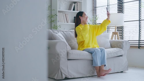 Happy young asian woman relaxing at home. Female smile sitting on sofa and holding mobile smartphone. Girl using video call to friend