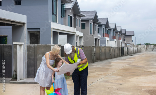 Senior construction foreman with beard using blueprint to explain a mother and her daughter for the detail of house building during the site check.