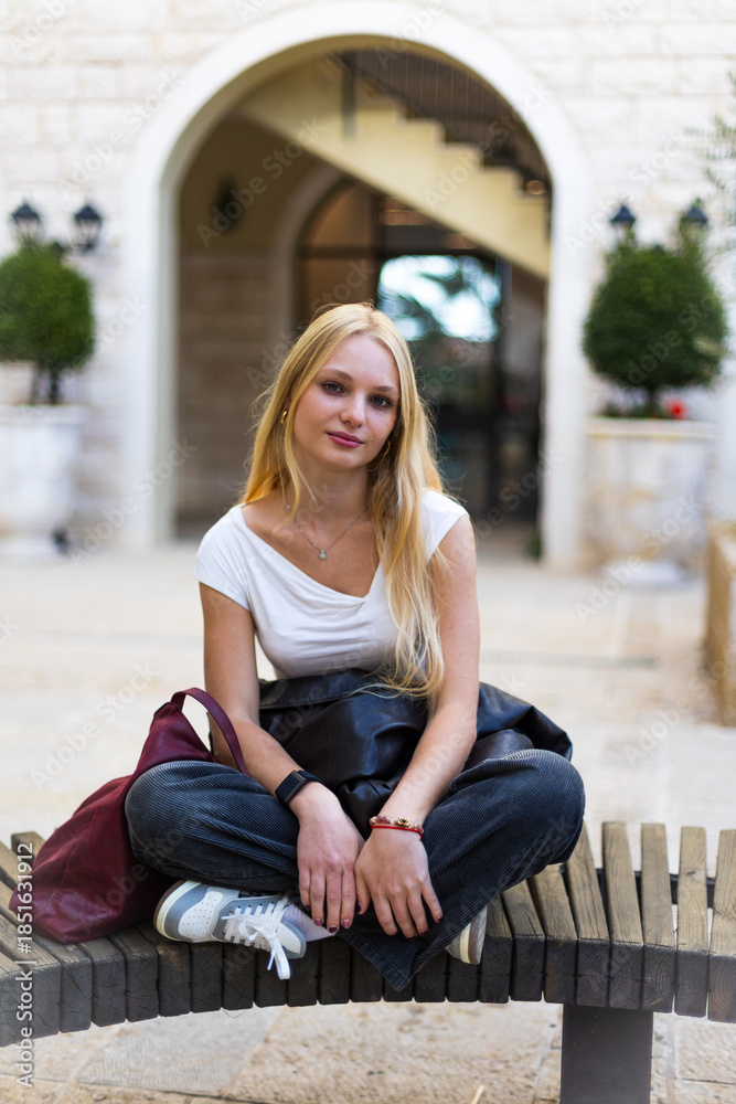 Fototapeta premium Stylish girl. A beautiful young blonde in fashionable clothes on a city street with a building in the background.