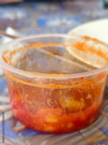 Фотография Used plastic container with red-orange food residue, indicating meal remnants and food storage practices
