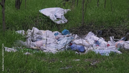 A pile of plastic waste and bottles lies dumped illegally in green forest grass. The scene highlights environmental pollution and soil contamination in nature.