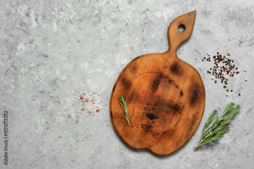 An empty round wooden cutting board with spices and rosemary on a rustic gray background. Minimal culinary backdrop. Top view, flat lay, copy space.